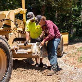 Two crew members servicing a motor grader