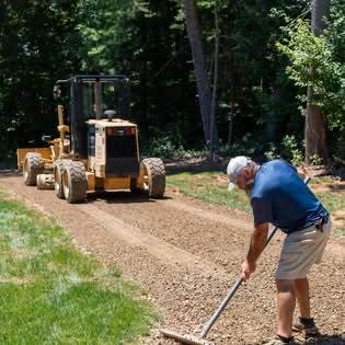 Crew member raking stone behind a motor grader