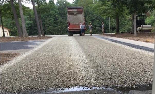 Dump truck spreading stone over fresh tar during a surface treatment job